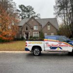 A roofing contractor's truck is parked in front of a house.